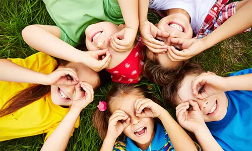 Wesołe dzieci leżą na trawie i robią okulary z rąk.